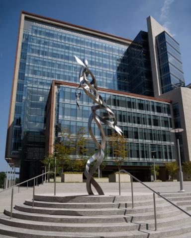 Silver metal sculpture on a staircase in front of a glass building