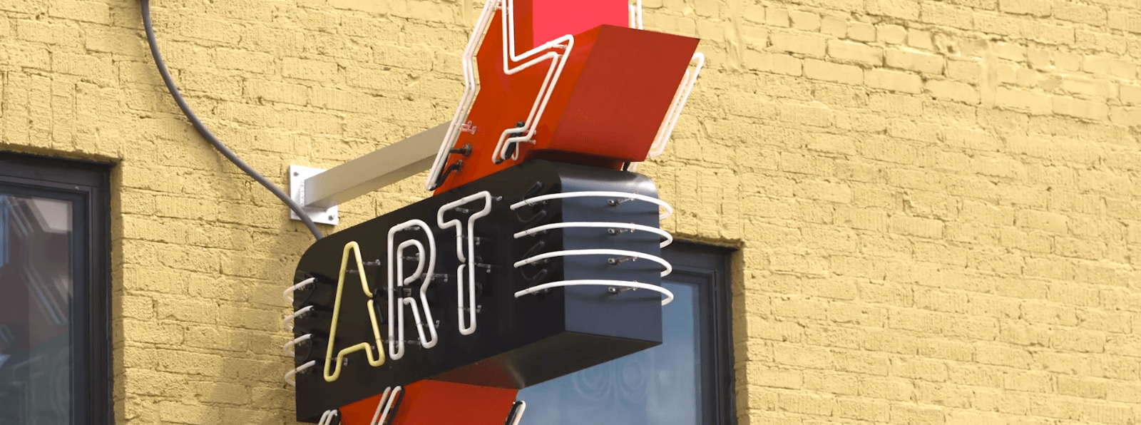 A marquee sign hangs on a brick wall reading ART with an arrow facing down