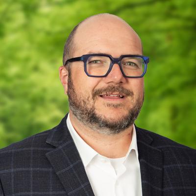 Ryan Patterson headshot. Smiling man with glasses, a mustache and beard, and wearing a dark sport coat over a white shirt.