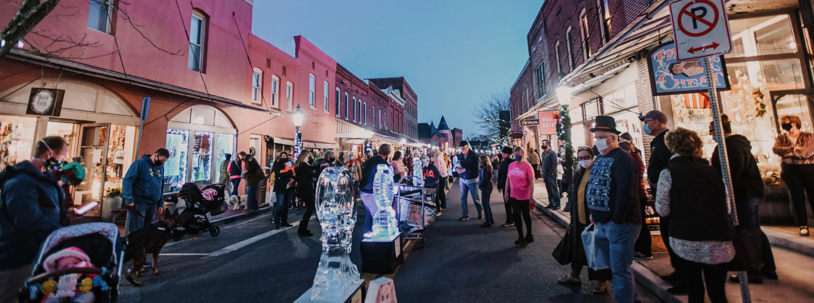 A crowd of people are staring at ice sculptures in the middle of the street at night.