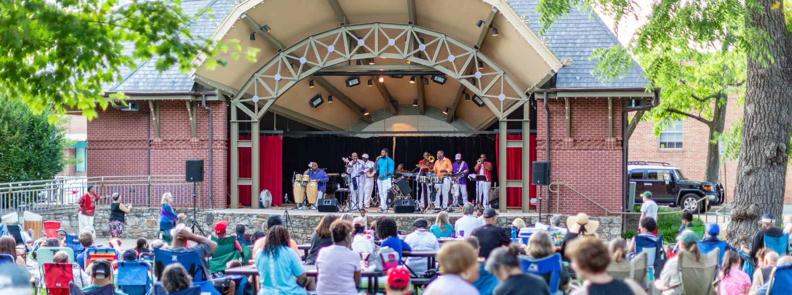 A crowd of people are listening to musicians performing on an outdoor stage.